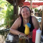 Ginger sitting in a tropical bar holding a mango daiquiri with an umbrella in it.