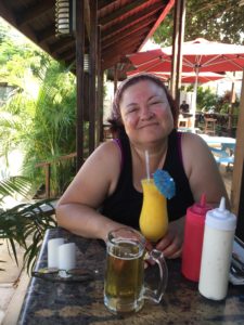 Ginger sitting in a tropical bar holding a mango daiquiri with an umbrella in it.